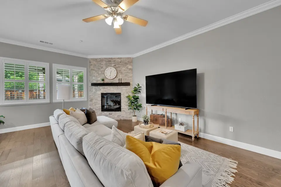 Family room seating beneath a ceiling fan, with a stone fireplace and windows looking outside.