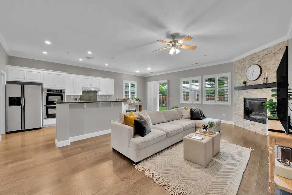 View across the family room toward the kitchen, with wood-look flooring and a stone fireplace.