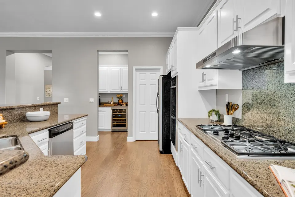 Kitchen aisle with white cabinets, gas cooktop, stone counters and a serving area beyond.