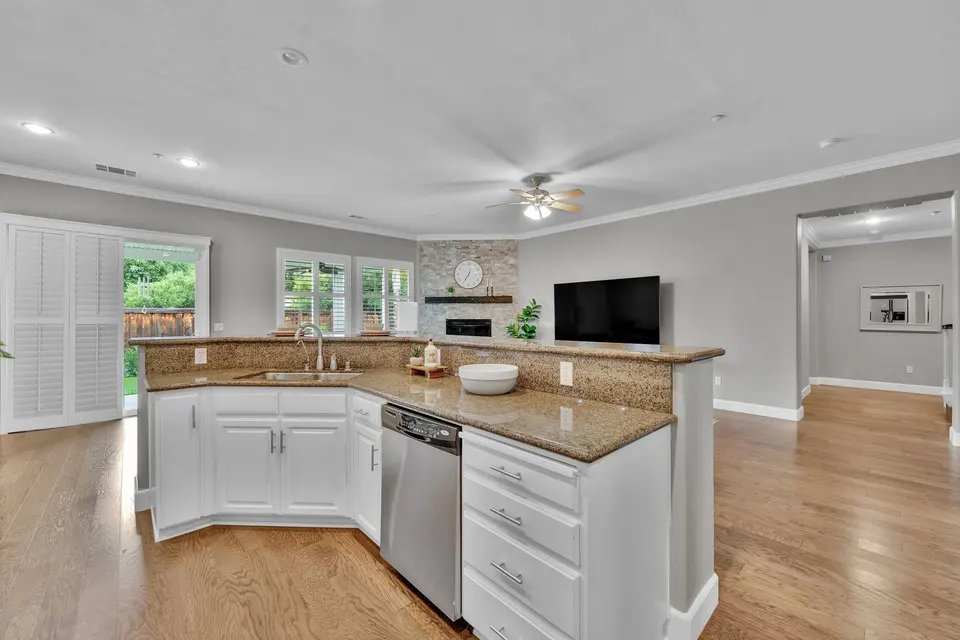White kitchen cabinets and a raised stone breakfast bar with views into the family room.