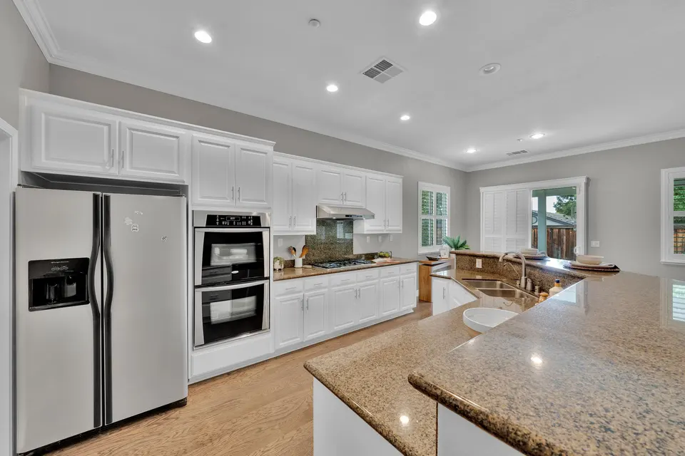 Kitchen with stainless refrigerator, double wall ovens, white cabinets and stone counters.