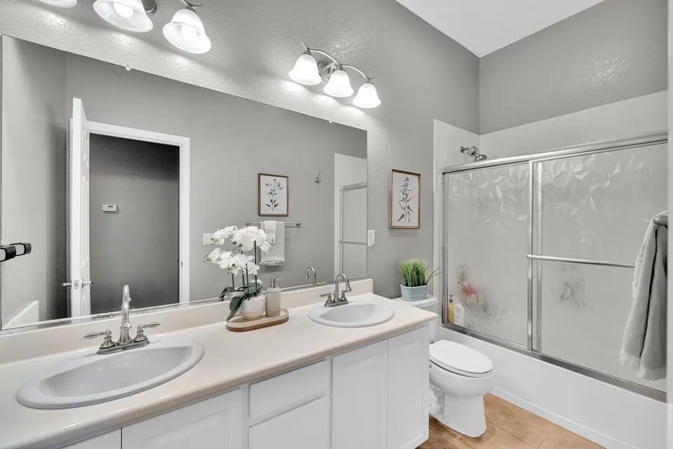 Main-level bathroom with two sinks, a wide mirror and a tub with sliding glass doors.