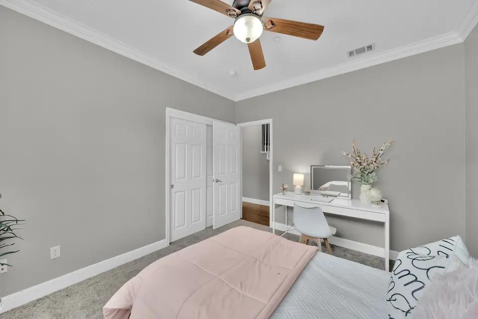 Secondary bedroom showing its closet doors, ceiling fan and desk beside the bed.