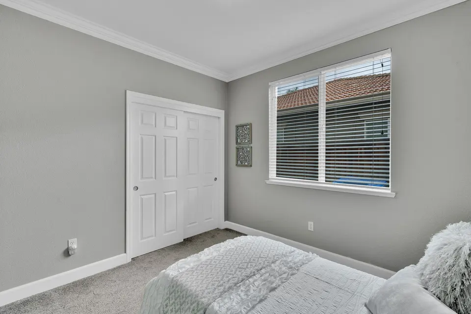 Reverse angle of a secondary bedroom showing a closet and window beside the bed.
