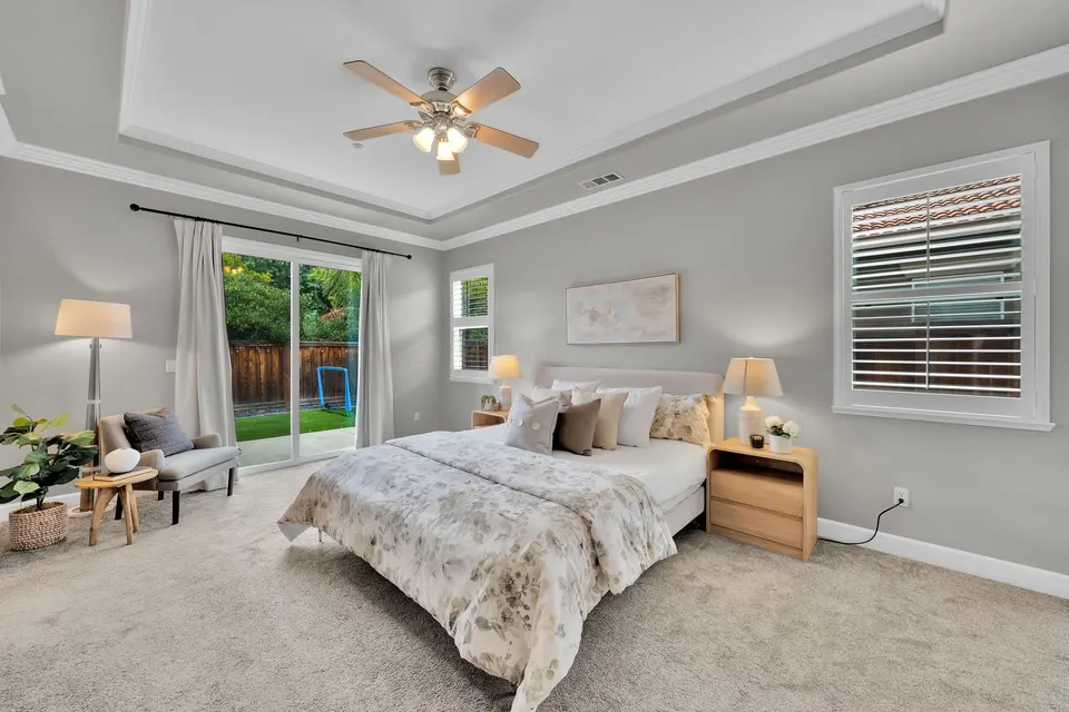 Primary bedroom with a tray ceiling, ceiling fan and sliding glass door to the backyard.