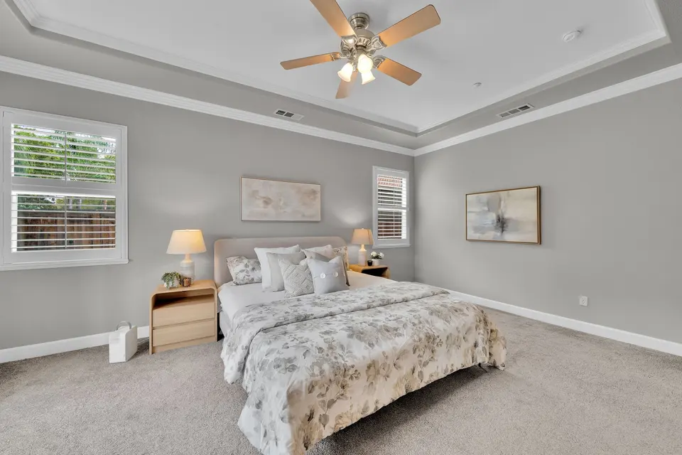 Primary bedroom with a tray ceiling, ceiling fan, two windows and room around the bed.