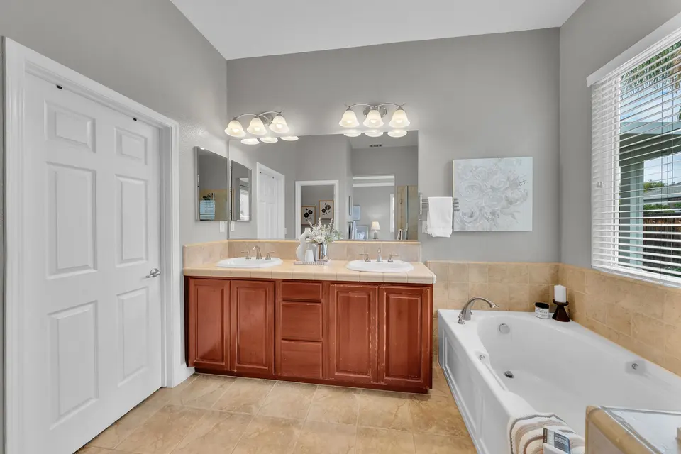 Primary bathroom with a double-sink vanity, bathtub and closet doors.