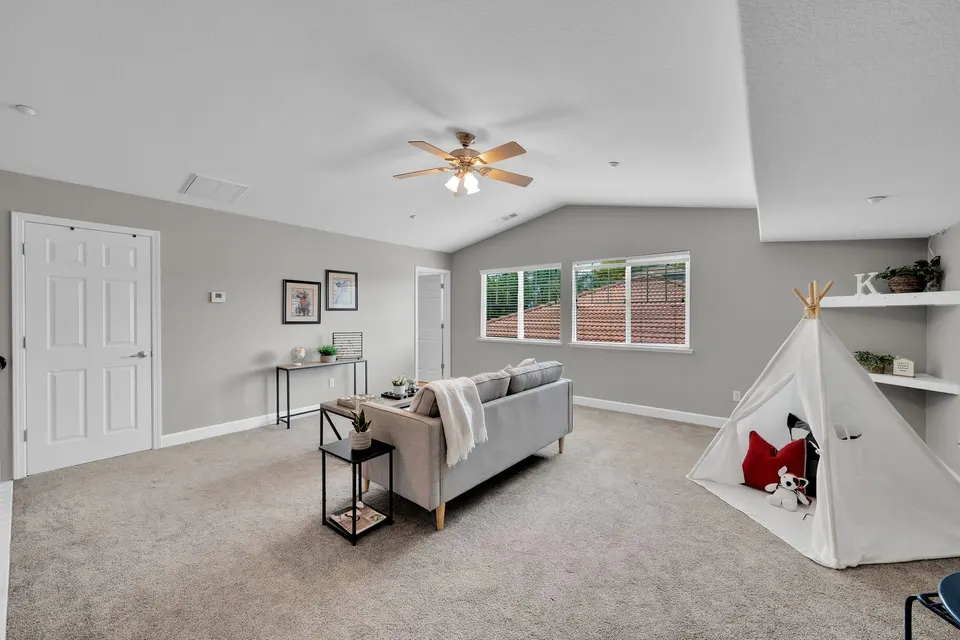 Upstairs loft with carpet, windows, seating and open space beneath a ceiling fan.