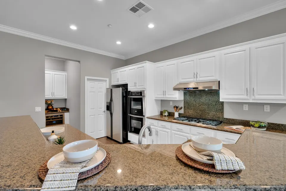 Kitchen with white cabinets, stainless refrigerator, double ovens and stone counters.