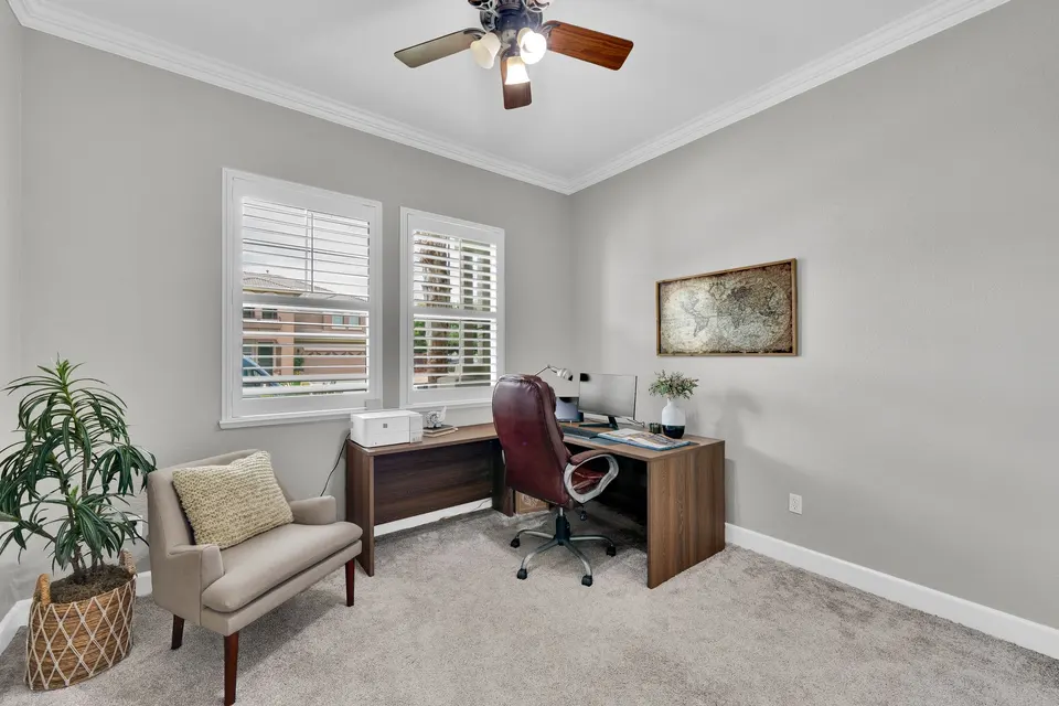 Additional room arranged as a home office, with a ceiling fan and shuttered windows.