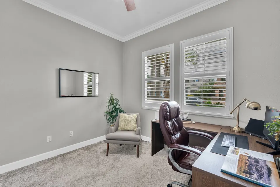 Reverse angle of the room shown as a home office, with shuttered windows and a desk.