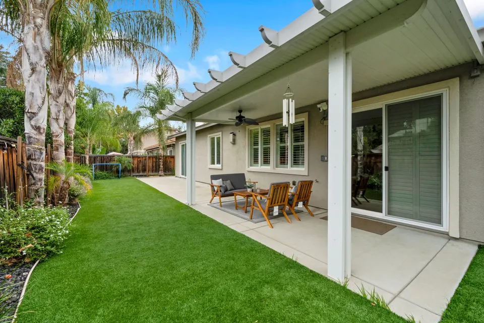 Backyard lawn with palm trees and a covered patio stretching along the rear of the home.