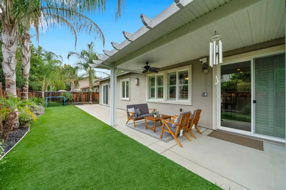 Backyard lawn and covered patio with seating, ceiling fan and sliding doors to the house.