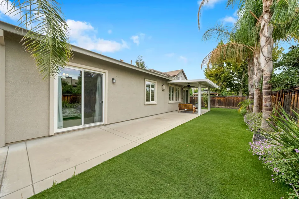 View along the backyard lawn and wide patio toward the covered outdoor sitting area.