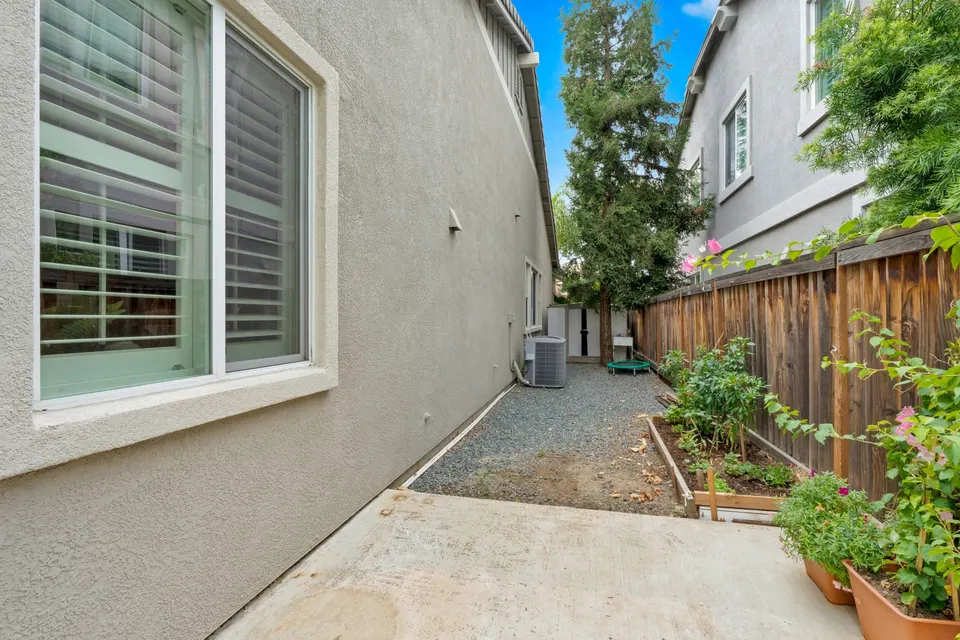 Side yard with a paved path, garden bed, fence and air-conditioning unit beside the house.